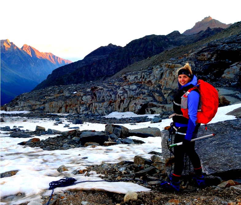 Woman with backpack by river with mountains behind