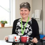Female smiling holding a tray of mugs