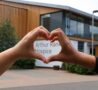 Hands in a heart shape in foreground with Hospice in background