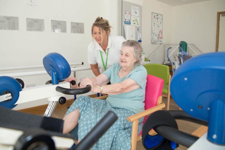 Woman exercises on Medimotion bike, supported by Therapist