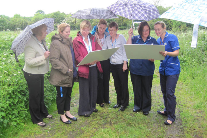 7 females under umbrellas looking at plans outside