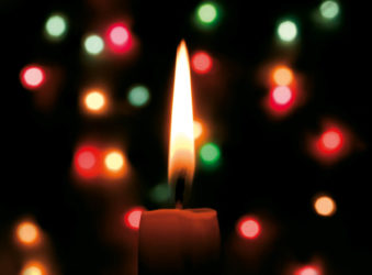 Candle at night with green red and yellow Christmas lights behind it