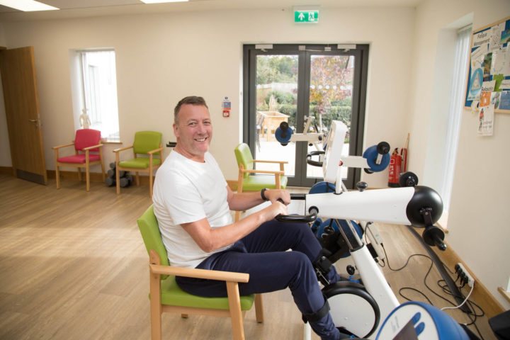 Patient smiles whilst using Medimotion Bike in physiotherapy gym