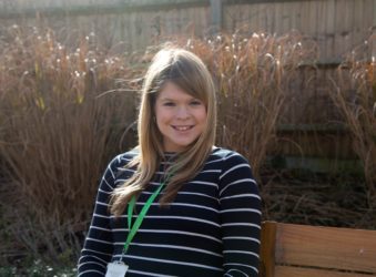 Female sitting on a bench with the sun behind her, smiling at the camera