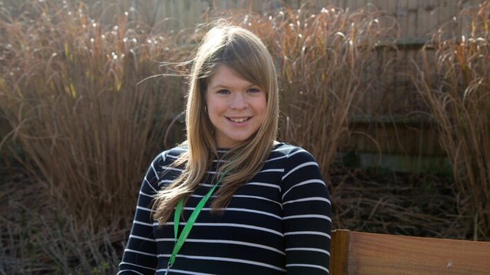 Female sitting on a bench with the sun behind her, smiling at the camera