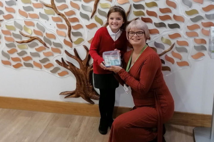 Young girl handing over lunchbox with donations to Community Fundraiser at the Hospice