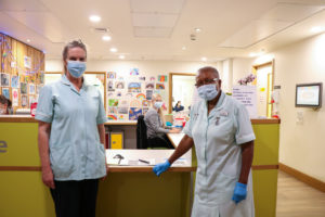 Two of the Hospice's healthcare assistants with one of the ward clerk's on the Inpatient Unit, with rainbow pictures behind