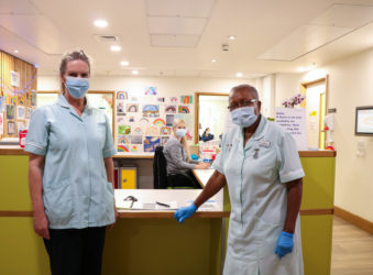 Two of the Hospice's healthcare assistants with one of the ward clerk's on the Inpatient Unit, with rainbow pictures behind