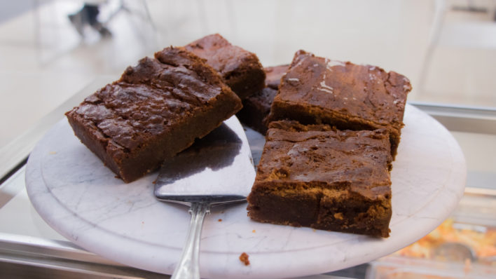 Four mouthwatering chocolate brownies with a cake slice under one, ready to be served