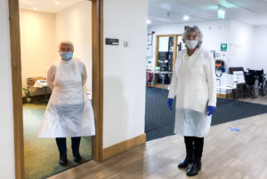 Two volunteers near the entrance of the Hospice in PPE, preparing for visitors' lateral flow tests