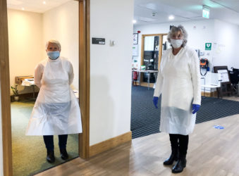 Two volunteers near the entrance of the Hospice in PPE, preparing for visitors' lateral flow tests