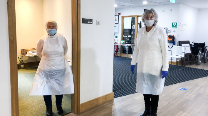 Two volunteers near the entrance of the Hospice in PPE, preparing for visitors' lateral flow tests
