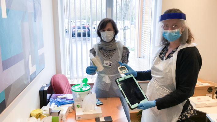 Two volunteers each in PPE displaying tablets, testing and cleaning kits