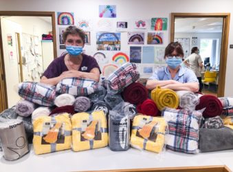 Doctor and nurse in scrubs with their elbows on piles of blankets donated to the Inpatient Unit