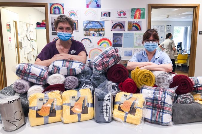Doctor and nurse in scrubs with their elbows on piles of blankets donated to the Inpatient Unit
