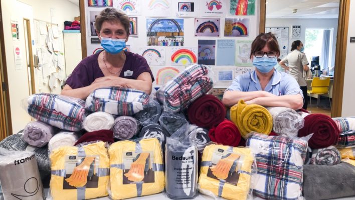 Doctor and nurse in scrubs with their elbows on piles of blankets donated to the Inpatient Unit