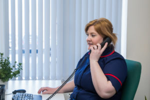 Nurse in dark blue uniform with red trim in office, answering telephone call