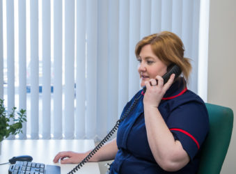 Nurse in dark blue uniform with red trim in office, answering telephone call