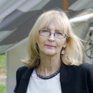 Informal portrait shot of Linda in a suit jacket, with her shoulder length blonde hair being blown behind her left shoulder