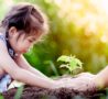 Parent's hands over those of a young girl tenderly planting shoot in freshly dug soil