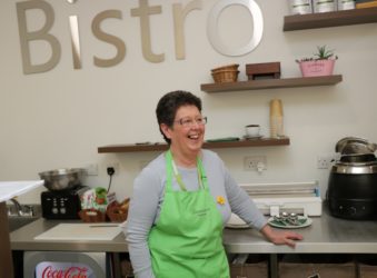 Lady volunteer standing in Bistro wearing a green apron and smiling