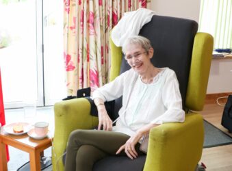 Laine sitting in the Day Therapy Lounge with her piece of cake and cup of tea
