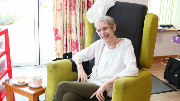 Laine sitting in the Day Therapy Lounge with her piece of cake and cup of tea