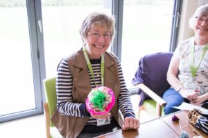 Female smiling at the camera holding a paper flower made at Arthur's Shed session at Arthur Rank Hospice Charity 