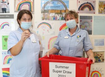 A nurse in the Inpatient Unit draws a ticket, as another holds the box of tickets for the Summer Super Draw 2021