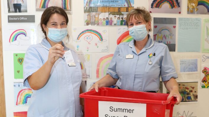 A nurse in the Inpatient Unit draws a ticket, as another holds the box of tickets for the Summer Super Draw 2021
