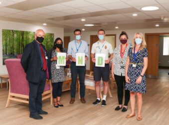 Members of the Addenbrooke's MND Clinic team, wearing masks and holding green letters 'M N D' in Bradbury Wellness Centre at the Hospice