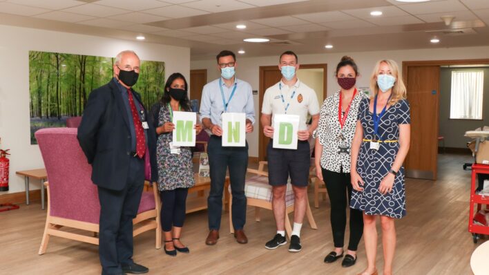 Members of the Addenbrooke's MND Clinic team, wearing masks and holding green letters 'M N D' in Bradbury Wellness Centre at the Hospice