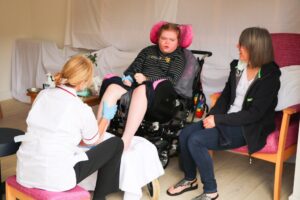 A young lady in a wheelchair enjoys a foot massage from one of the teams' complementary therapists, in Arthur's Shed