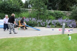 Young lady has a go at seated curling as family members and hospice colleagues cheer her on