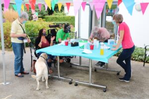 The arts and crafts table with a young man painting a cap, a PAT dog and staff, with colourful bunting in the foreground