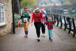 Female adults and young boy dressed up in red and green festive outfits walking near a river