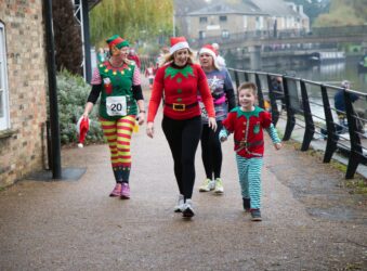 Female adults and young boy dressed up in red and green festive outfits walking near a river