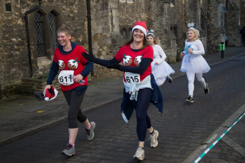 Female adults running and smiling wearing red and white Christmas pudding jumpers 