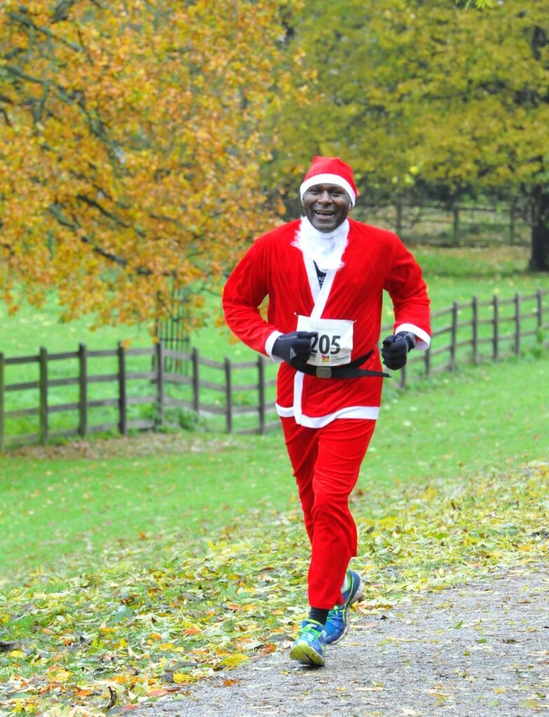 Male adult running in the park and smiling wearing a red and white santa outfit 