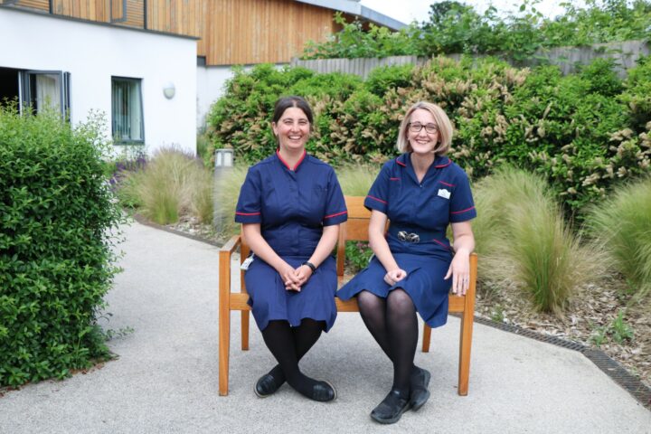 Two smiling female nurses sitting on a bench in the garden