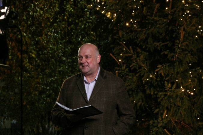 Male holding a book standing in front of a Christmas tree at night