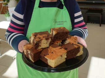 Female wearing a mask and green apron holding a plate of Chocolate Berry Marble Cake