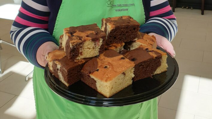 Female wearing a mask and green apron holding a plate of Chocolate Berry Marble Cake