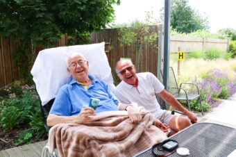 Gentleman eating icecream on decking of Bistro laughs with friend on a sunny day