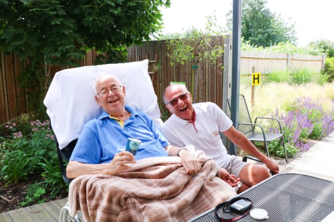 Gentleman eating icecream on decking of Bistro laughs with friend on a sunny day