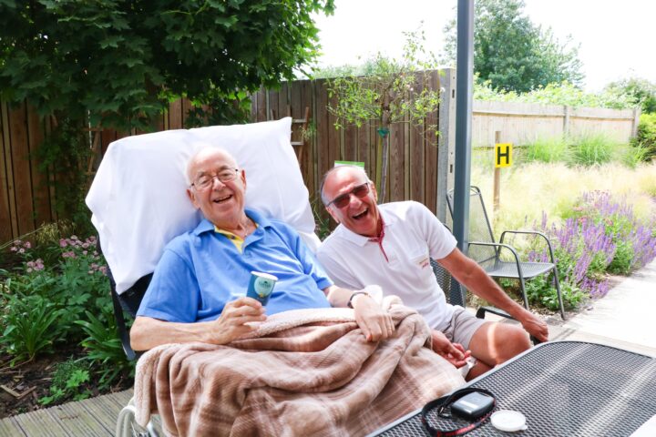 Gentleman eating icecream on decking of Bistro laughs with friend on a sunny day