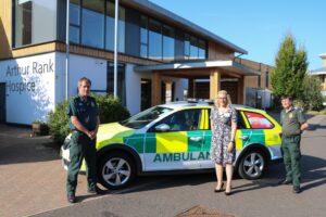 Director of Clinical Services, Sara Robins with members two members of EAAST and an ambulance car outside Arthur Rank Hospice Charity's Shelford based home