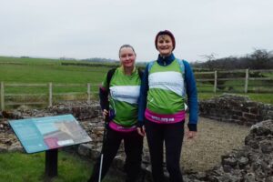 Females wearing green, white and pink Arthur Rank Hospice Charity t-shirt next to Hadrian's wall