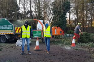 men wearing masks and high vis jackets near road cones in the woods shredding trees 