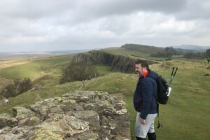 Male standing near Hadrian's Wall with green hills in the background